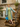 Woman posing on stone steps in 1940s sage green floral dress, mint coat, yellow beret, and blue handbag