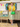 Blonde woman posing by vintage caravan wearing yellow Daydream cardigan and green bag