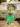 Model seated outside vintage caravan wearing powderpuff beige cardigan over a green dress