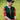 Blonde woman wearing forest green cable knit sweater vest over bright red floral tea dress